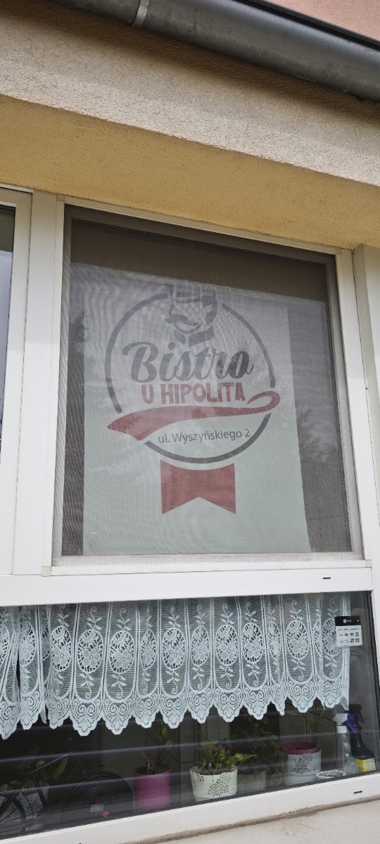 Okno z szyldem Bistro u Hipolita i koronkową firanką